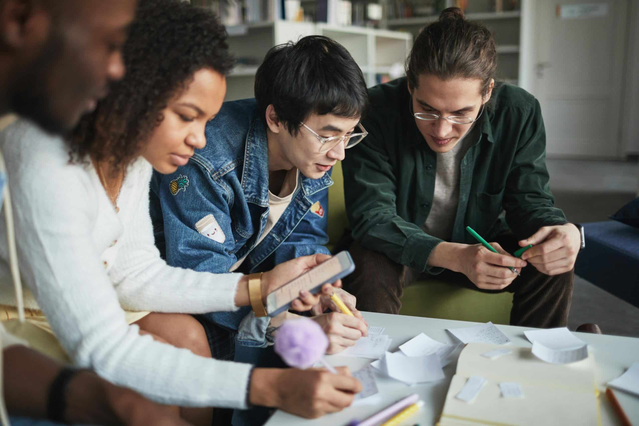 Multiracial group of college students working together on a project in a modern library setting.